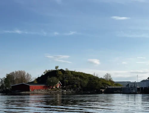 Im Vordergrund Wasser mit einem Gebäude und Hügel.
