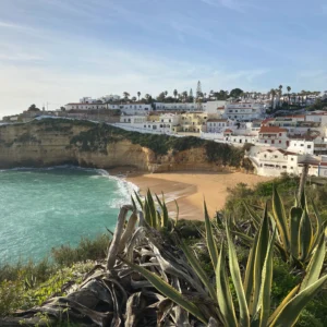 Algarve: Im Vordergrund Pflanzen, im Hintergrund ein Küstenort mit gleichnamigen Strand.